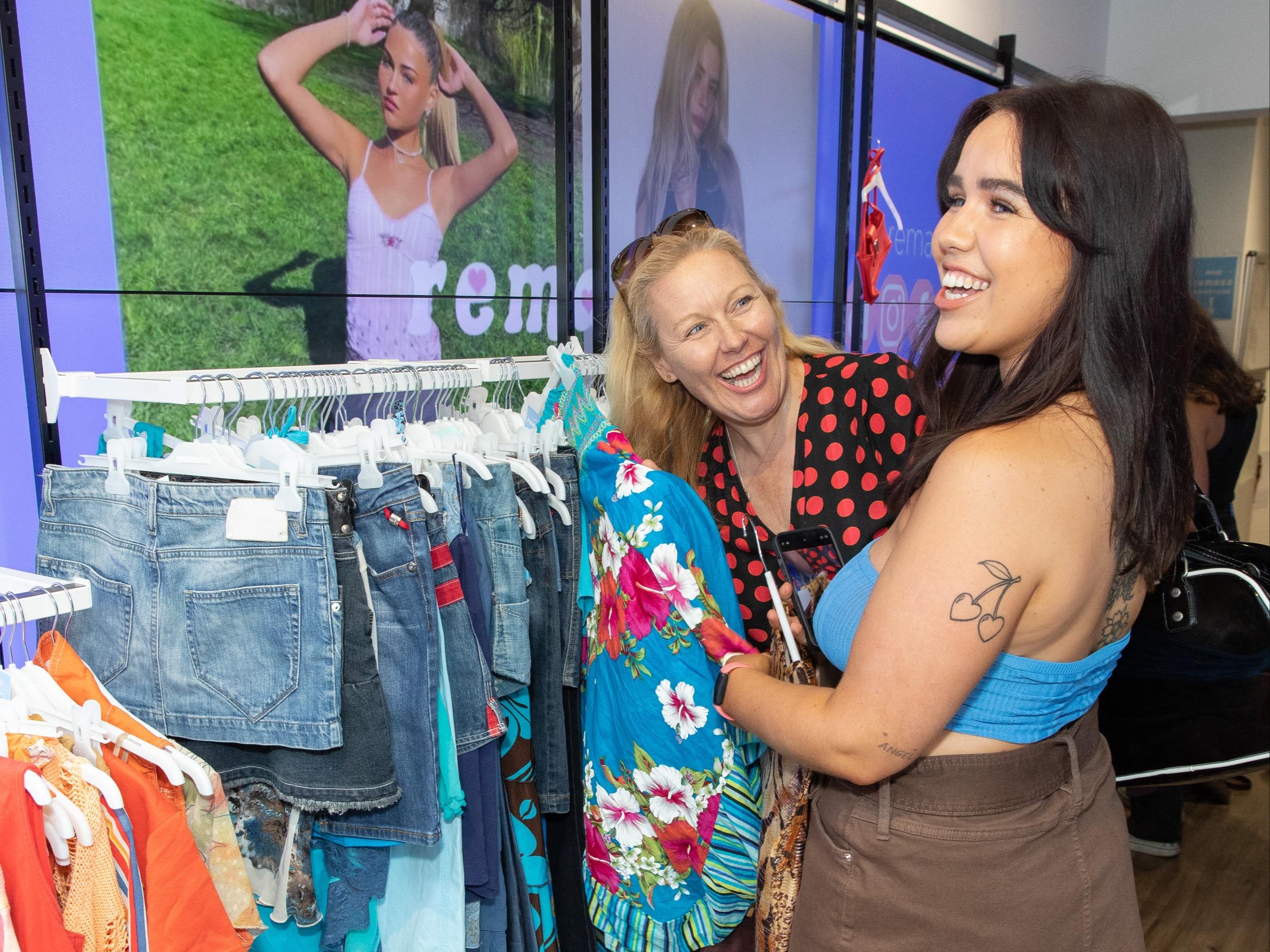 Two women laughing while picking out clothes from a rack